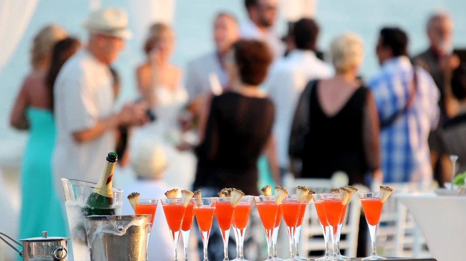 Scène extérieure de réception ou événement professionnel sur terrasse avec invités en tenue élégante socialisant en arrière-plan flou
