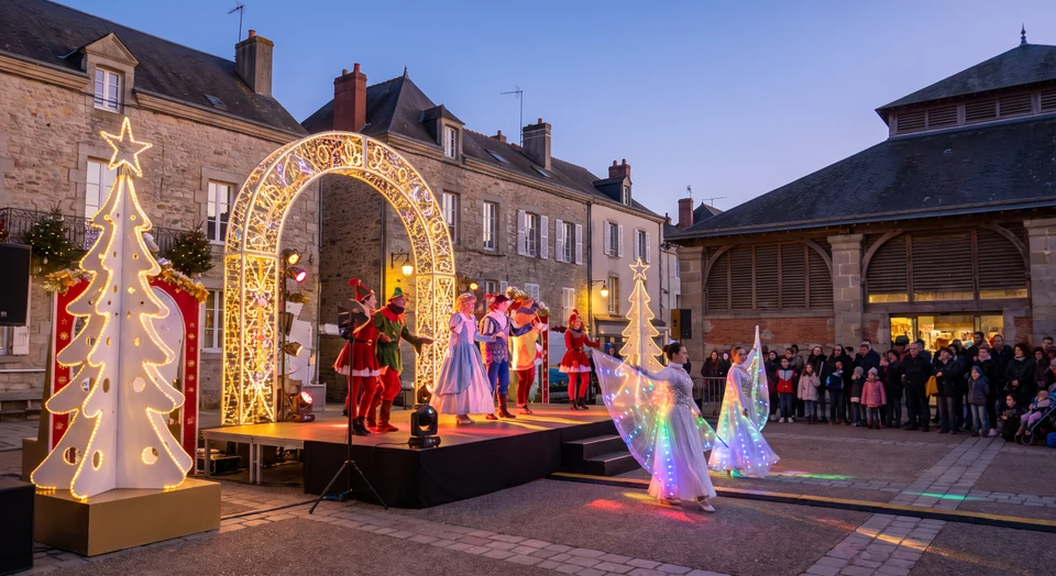 Photographie d'une scène de spectacle festif en intérieur ou extérieur, éclairée par des projecteurs colorés et des éléments de décor festif (structures décorées, guirlandes lumineuses, podium ou estrade). On peut voir un public attentif en arrière-plan ou des éléments de mise en scène professionnelle (son, lumière) en action, illustrant une création événementielle festive et marquante réalisée par une agence professionnelle.