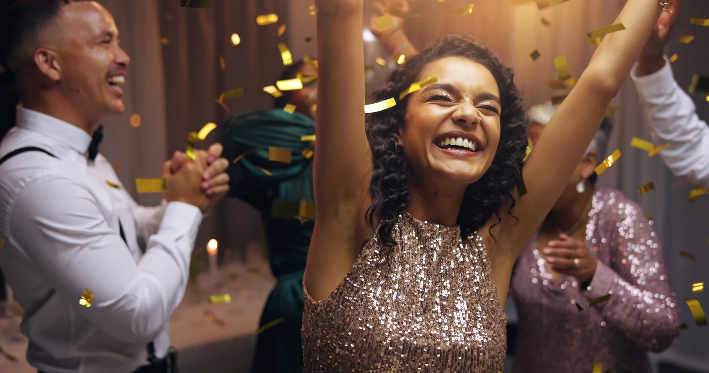 Scène festive d'intérieur avec confettis colorés voltigeant dans l'air au-dessus de chapeaux de fête coniques disposés sur une surface jonchée de papiers multicolores