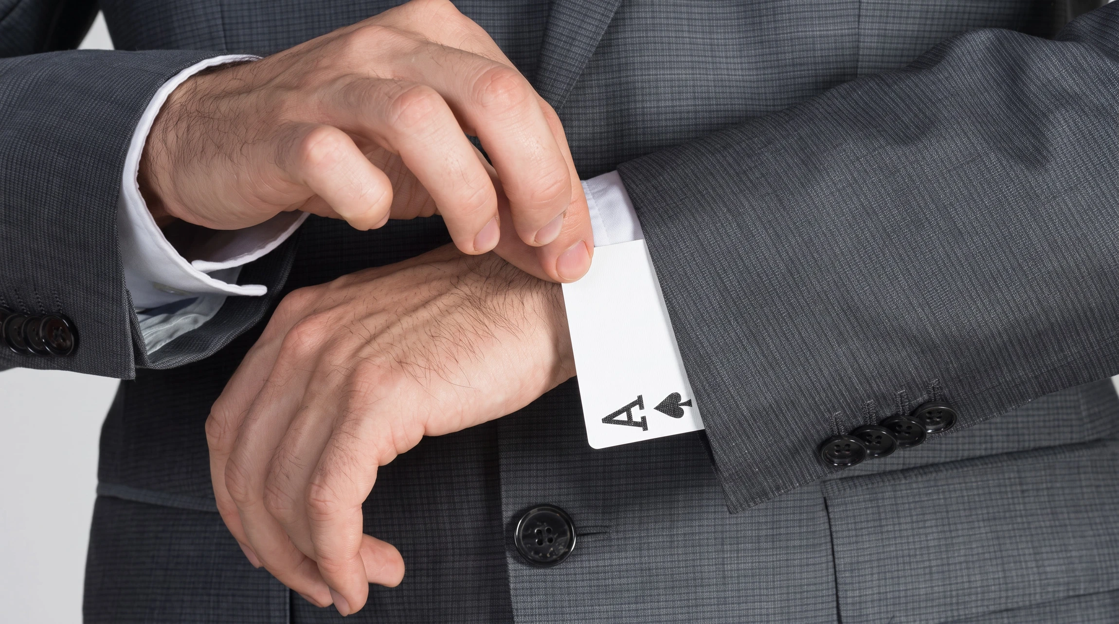 Un homme en costume gris anthracite sort discrètement un as de pique de sa manche lors d'une situation professionnelle ou de négociation d'affaires